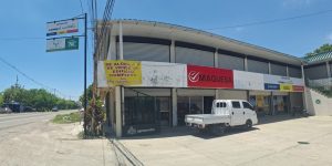 Commercial building with a red MAQUESA sign, a yellow 'For rent/For sale' banner, shuttered storefronts, and a white pickup parked out front on a sunny street.